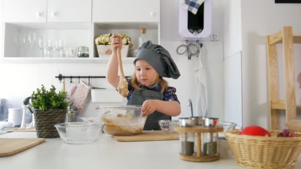 Preescolar niña panadero amasa la masa con una cuchara de madera grande en un tazón — Vídeos de Stock