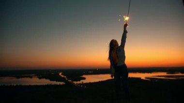 Mutlu genç kadın uzun saçlı maytap ile el üstünde belgili tanımlık tepe yaz gün batımında yükselterek rüzgarda uçan