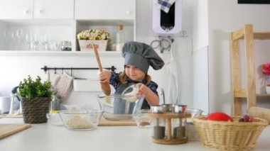 Okul öncesi kız baker bir kase büyük bir tahta kaşık ile hamur kneads