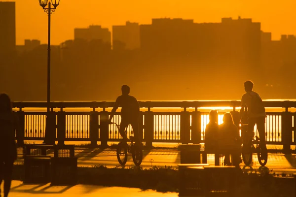 Sylwetki ludzi na cykle przy promenadzie o zachodzie słońca — Zdjęcie stockowe
