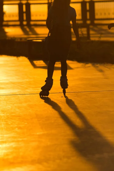 Silhueta de jovem mulher em patins no calçadão ao pôr do sol — Fotografia de Stock