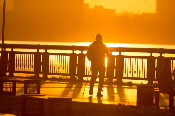 Мужской силуэт занимается спортивной ходьбой по набережной на ярком закате — стоковое фото