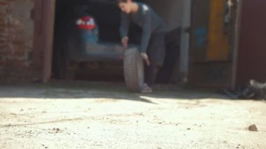 Genç adam sokağa tekerlek araba bagajında atıyor.