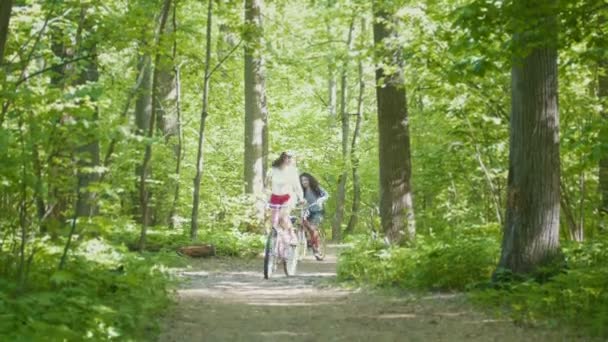 Две девушки катаются на велосипедах по дорожке в парке — стоковое видео