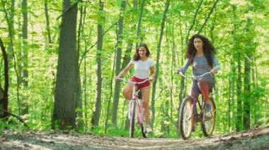 İki kız arkadaş güneşli bir günde yeşil orman bisiklet sürmek
