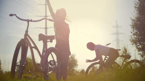 女の子が森の中の太陽を背景に自転車で歩く前に演習を行う — ストック動画