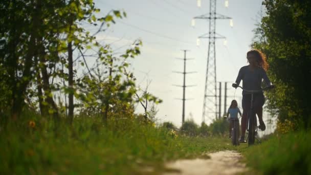 Дві брюнетки-велосипедисти плавно проходять по шляху на тлі блакитного неба і зелених дерев — стокове відео