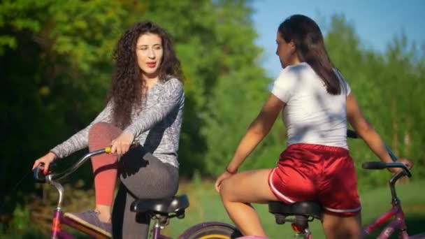 Два молодых велосипедиста общаются и смеются в велосипедной поездке в парке, в солнечный летний день — стоковое видео