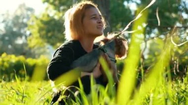 Parkta çimlere oturup, küçük bir köpek tutarak ve onu okşayarak kız