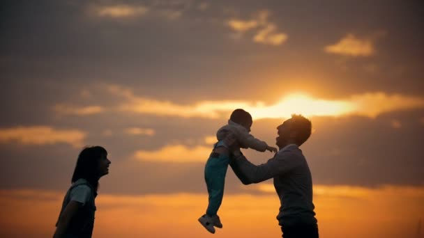 Eltern werfen ihren Sohn in die Luft, ein Sommerabend, Sonnenuntergang — Stockvideo