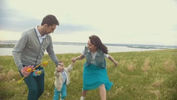 Mama und Papa halten die Kinder an den Händen und heben ihn auf, eine junge Familie bei einem Spaziergang auf dem Feld, bewölktes Wetter — Stockvideo