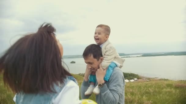 Mamãe e papai brincando com a criança no campo, pulando, papai segurando o bebê em seus braços, nublado — Vídeo de Stock