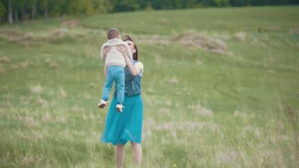 Мама обнимает ребенка и кружится с ним, летняя прогулка по полю, облачный день — стоковое видео