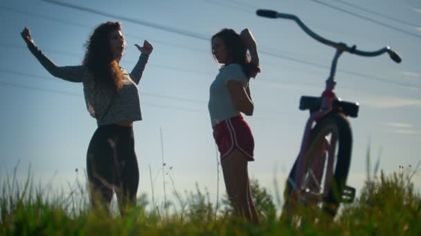 Dos chicas jóvenes se calientan, saltar antes de un paseo en bicicleta, día soleado — Vídeos de Stock