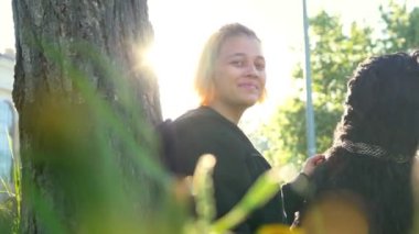 Yakınındaki bir ağaç güneş ışığı binada karşı parkta oturan bir köpek olan genç bir kadın