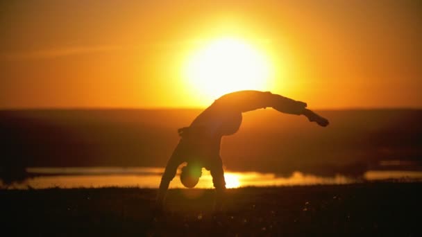Deportista se dedica a la capoeira en el fondo de una puesta de sol naranja, en cámara lenta — Vídeo de stock
