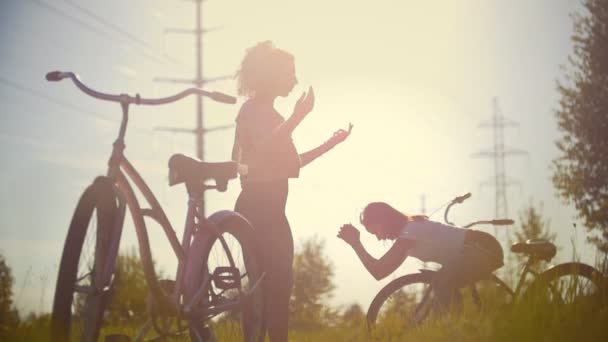 Meninas-ciclistas manter um ao outro e se aquecer em pakr, ao lado de suas bicicletas, verão dia ensolarado — Vídeo de Stock