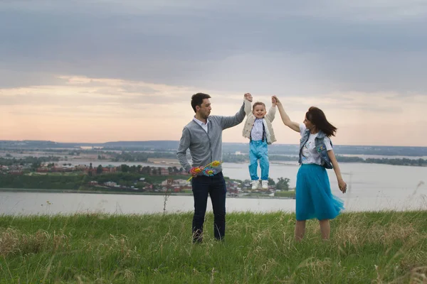 Родители держат своих сыновей за руки и поднимают, ребенок прыгает, облачно — стоковое фото