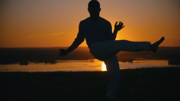 Un uomo esegue tecniche di combattimento sullo sfondo del sole al tramonto, al rallentatore — Video Stock