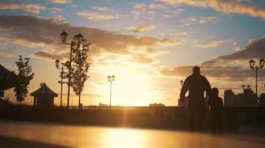 Adam adam taşıyan genç kadın bir tekerlekli sandalyede geçmiş quay, günbatımında yürüyen bir çocuk ile