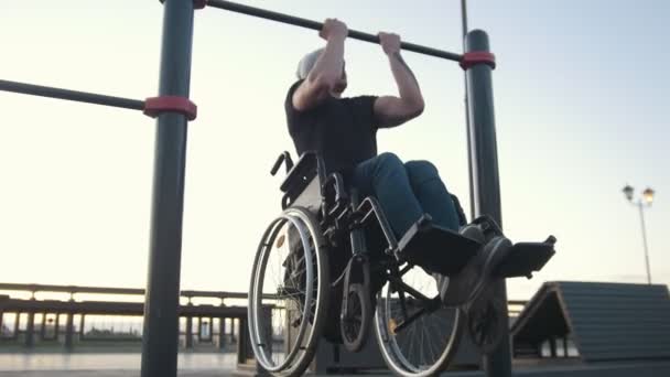 Young disabled man in wheelchair engaged on the crossbar outdoors — Stock Video