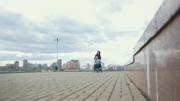 Hombre discapacitado en silla de ruedas con una mujer joven caminando por la calle de la ciudad — Vídeos de Stock