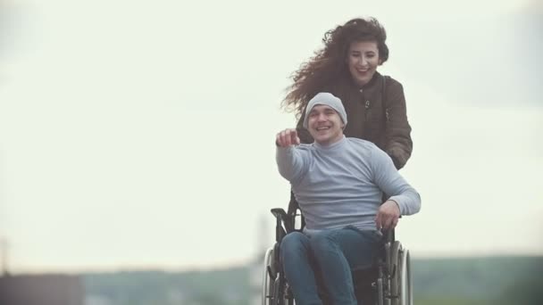Happy gehandicapte man in een rolstoel met gelukkige jonge vrouw lopen bij de stad straat — Stockvideo
