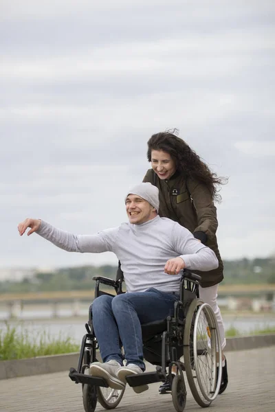 Інвалідний чоловік у інвалідному візку з молодою жінкою, що йде по міській вулиці — стокове фото