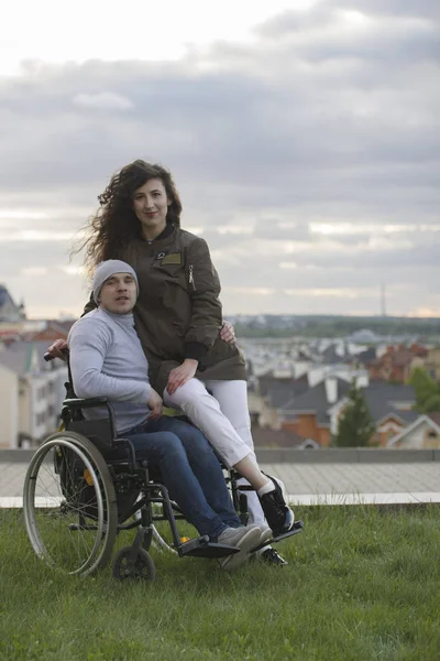 Porträt eines glücklichen behinderten Mannes im Rollstuhl umarmt junge Frau im Freien — Stockfoto