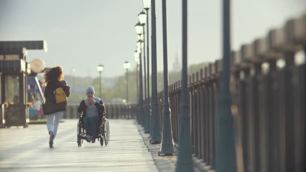 Un homme handicapé en fauteuil roulant prend des photos d'une jeune femme au quai — Video