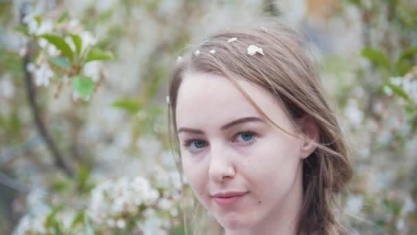 Портрет молодой женщины в саду - девушка засовывает веточку сирени в волосы — стоковое видео
