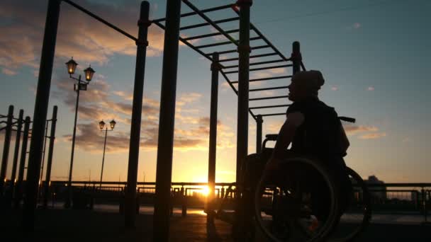 Silhouette de jeune homme handicapé tiré sur les traverses au coucher du soleil à l'extérieur — Video