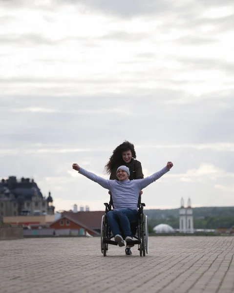 Молода жінка з щасливим інвалідом в інвалідному візку розважається на відкритому повітрі — стокове фото