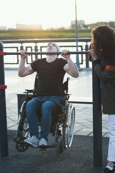 Сильний інвалідний чоловік у інвалідному кріслі піднявся на бар біля молодої жінки на заході сонця — стокове фото