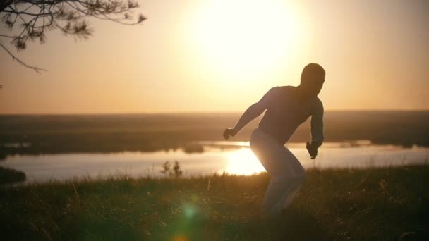 Mladík akrobatické provádí bojové triky na kopci při západu slunce — Stock video