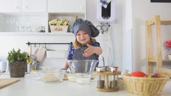 Веселая маленькая девочка в фартуке выкатывает тесто на кухне — стоковое фото