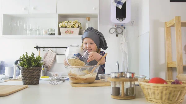Маленькая девочка добавляет ингредиенты в тесто — стоковое фото