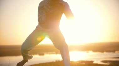 Erkek siluet Capoeira öğeleri üstünde belgili tanımlık tepe yaz gün batımında gerçekleştirme.
