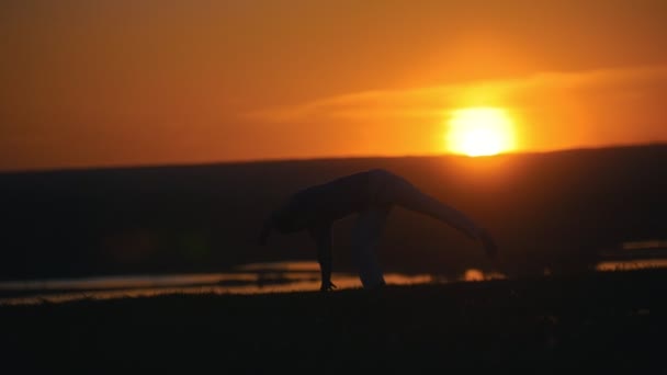 Silhouette de combattant homme effectuant des flips sur la colline au coucher du soleil d'été — Video