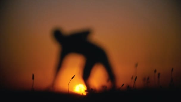 De-focused silhouette of male fighter performing capoeira tricks on the hill at sunset — Stock Video