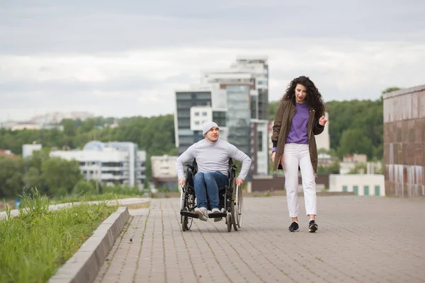 Young woman with happy disabled man in wheelchair having fun outdoors