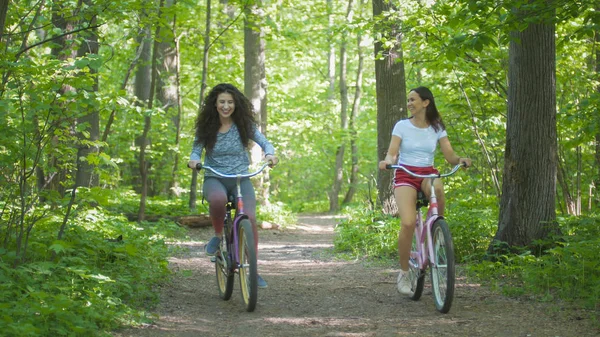 Two girls climb the path to the hill in the green forest, one girl falls, summer day
