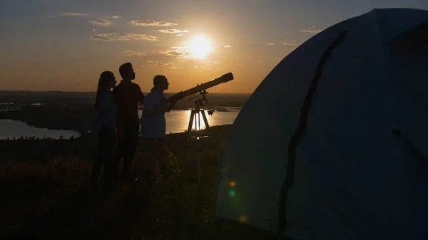 Joven mostrando a sus amigos una hermosa vista a través del telescopio al atardecer de verano —  Fotos de Stock