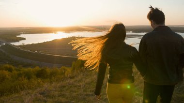 Genç çift elele günbatımında bir alanda yürüyüş