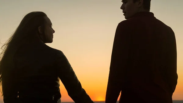 Liefdevolle jonge paar hand in hand elkaar kijken naar geweldige zonsondergang buitenshuis - close up — Stockfoto