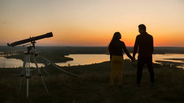 望远镜站在情侣面前, 在山上牵手在惊人的日落 — 图库照片