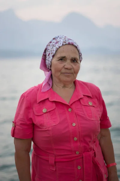 Портрет пожилой улыбающейся женщины у моря на фоне гор — стоковое фото