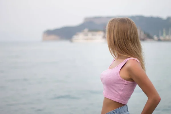 Portrait d'une jeune femme blonde méconnaissable regardant la montagne au bord de la mer — Photo