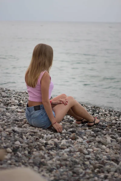Vue arrière de la jeune femme blonde assise sur le bord de mer en pierre — Photo