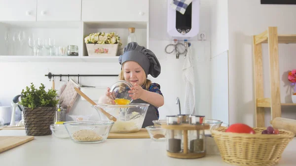 Веселая маленькая девочка в фартуке выкатывает тесто на кухне — стоковое фото